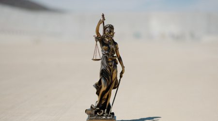 Een foto van een beeldje van Vrouwe Justitia bij een juridisch artikel.